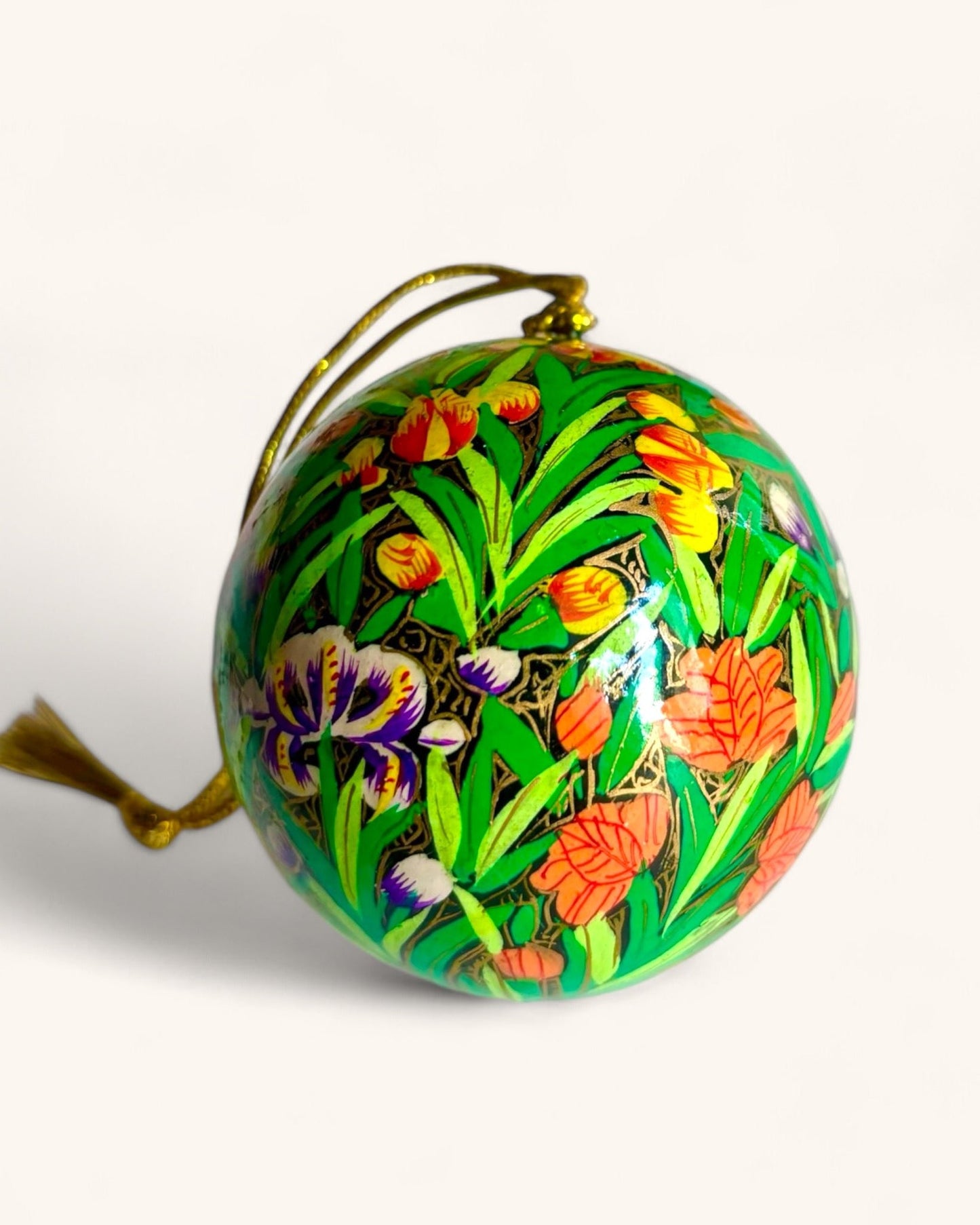 Primo piano di una pallina di Natale decorata a mano con motivi di tulipani e foglie su sfondo verde.