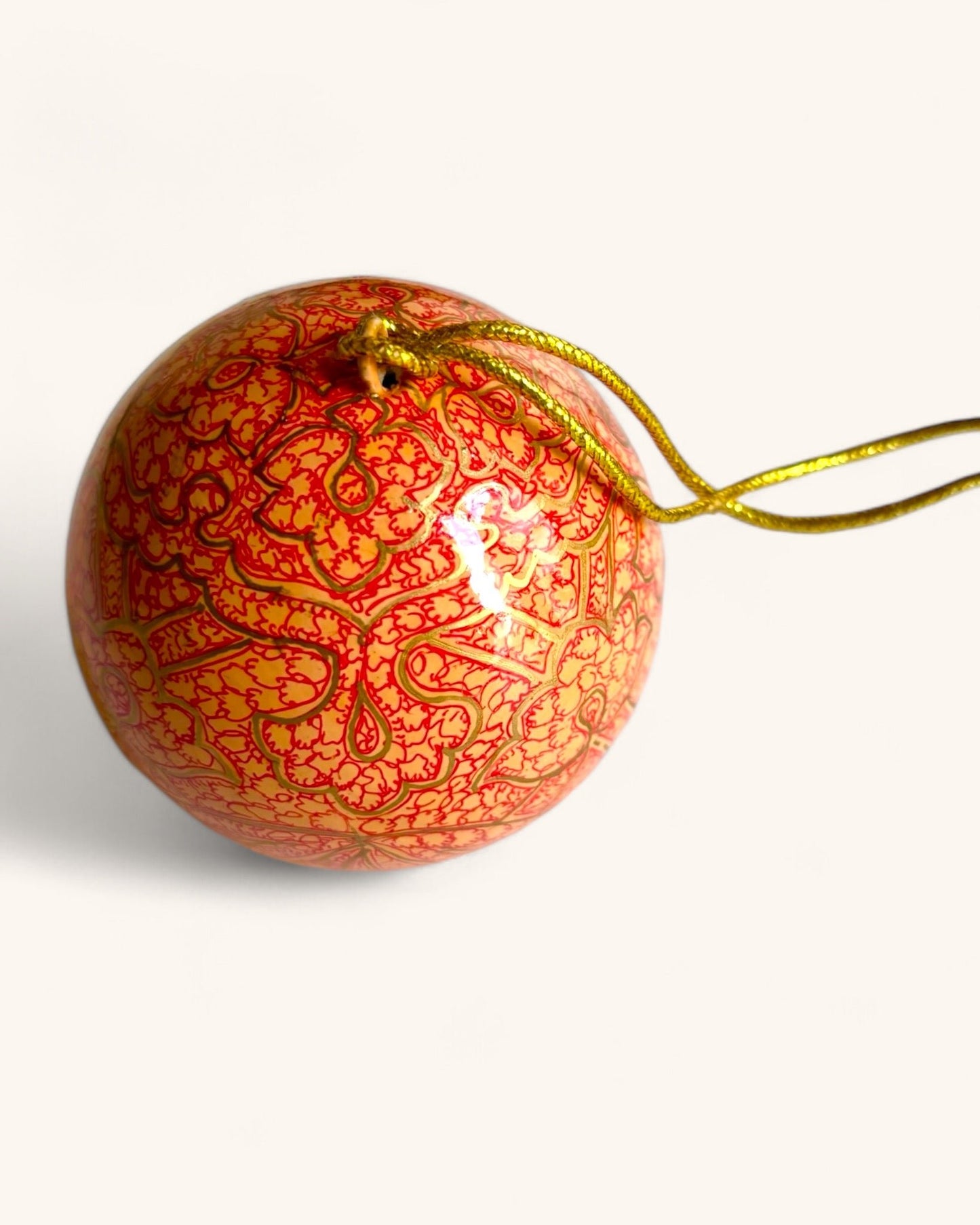 Dettaglio della pallina Arabesque per l'albero di Natale, design esotico con motivi intricati dorati e rossi su sfondo arancio-pesca.