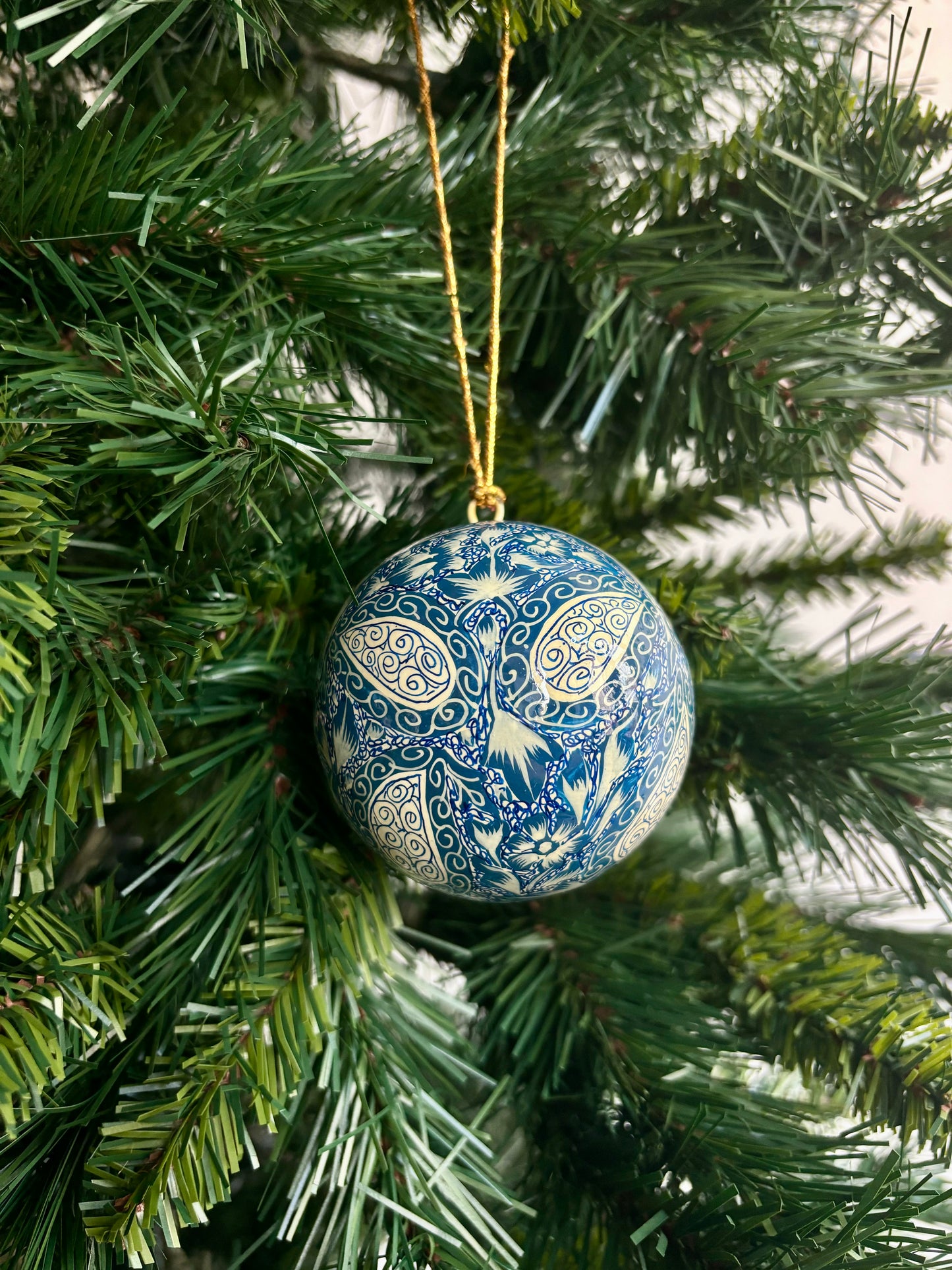 Decorazione natalizia in papier maché blu cobalto con motivi bianchi ispirati all'arte tradizionale del Kashmir.