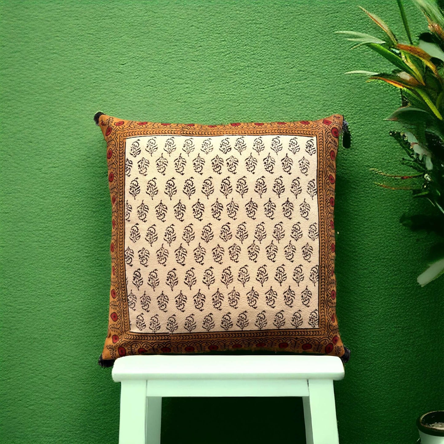 Copricuscino beige elegante con dettagli artigianali e pompom neri agli angoli.