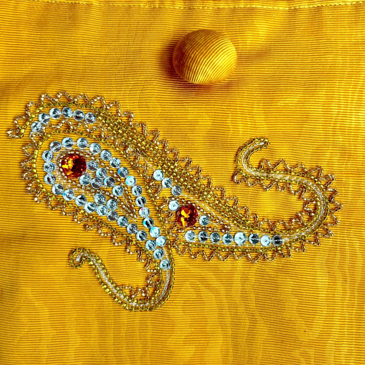 Dettaglio del ricamo cachemiere con cristalli gialli e ambra su borsa in tessuto moiré ondulato.