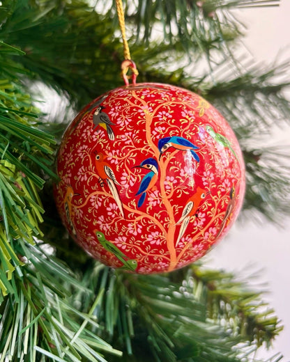 Palline di Natale in papier-mâché con design dipinto a mano, ispirate alla natura e agli uccelli selvatici, su sfondo decorativo.