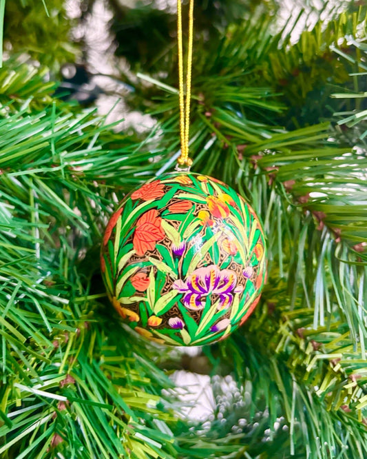 Pallina di Natale elegante con decorazioni floreali multicolore, appesa a un ramo di abete.