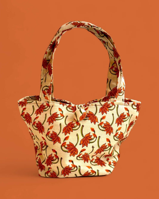 Borsa Daisy in cotone con stampa block-printing floreale arancione su fondo crema, design trapezoidale elegante.