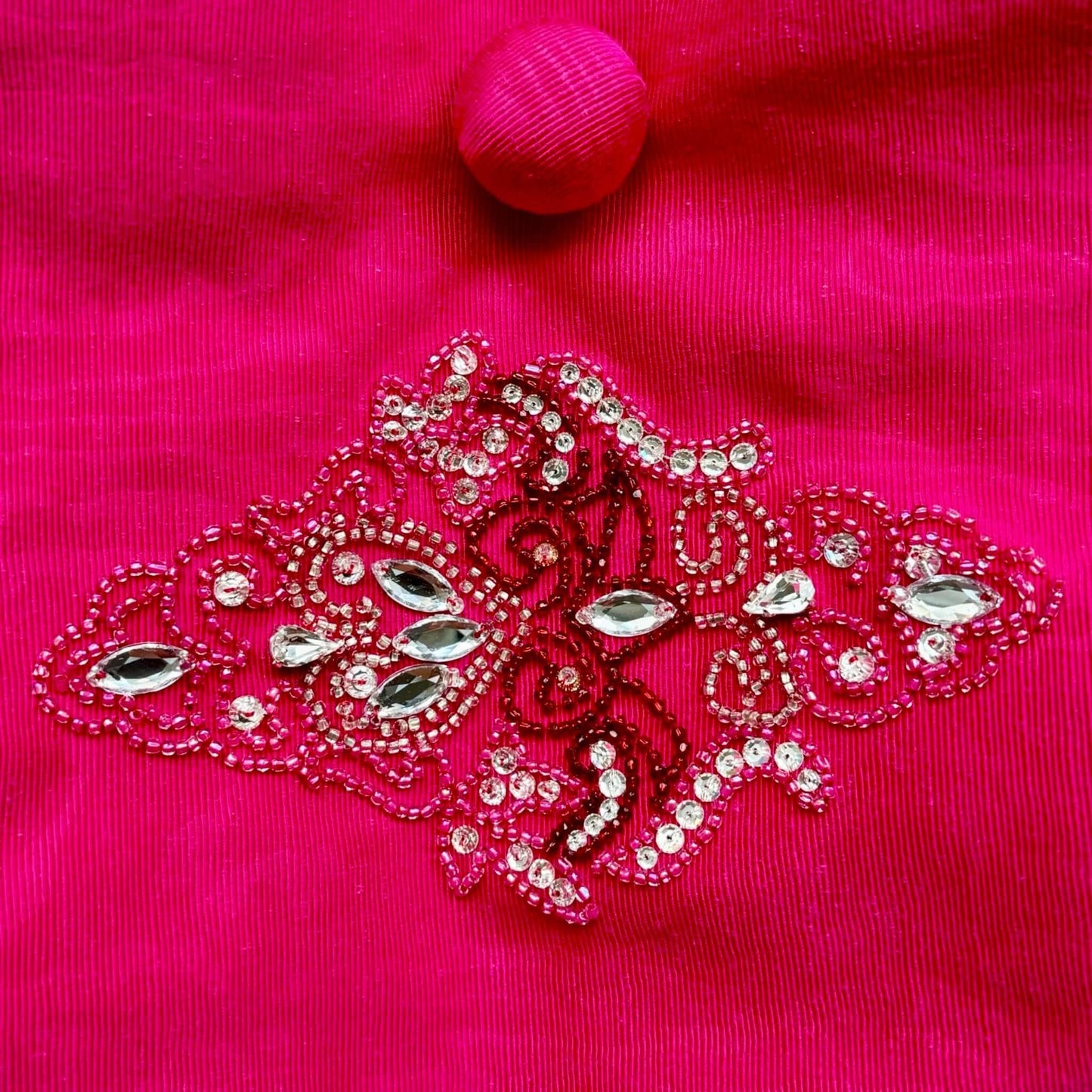 Ricamo a mano con pietre e strass su borsetta da sera fucsia.