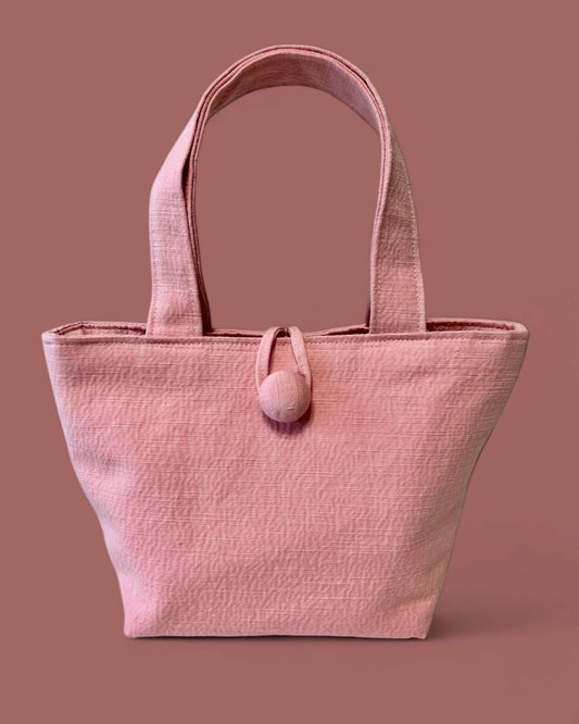 Minibag in tessuto ottoman rosa con design a trapezio rovesciato e texture a coste sottili, perfetta per un look da città elegante e versatile.